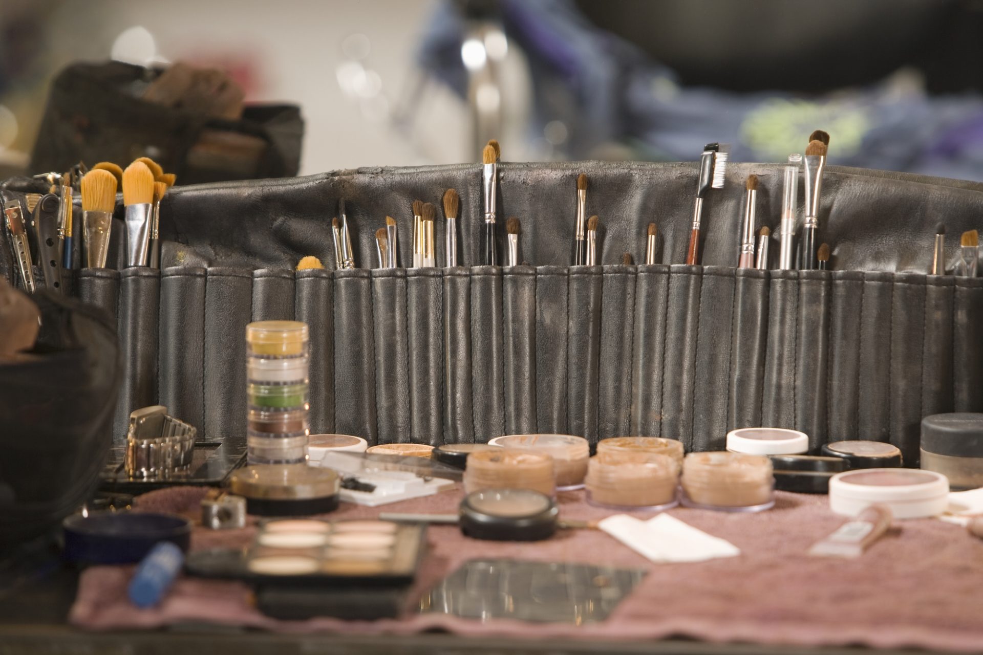 Professional makeup brushes laid out in a roll beside a kit on a table