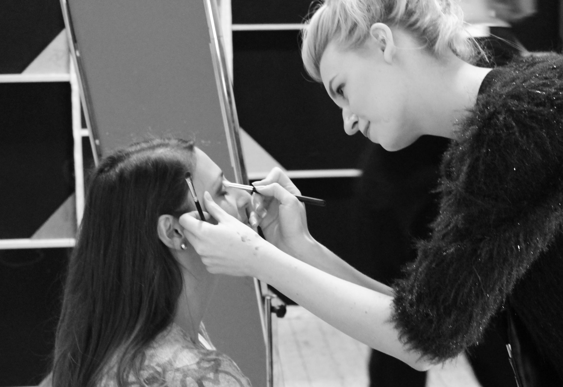 Black and white photo of a makeup artist applying eye makeup to a client