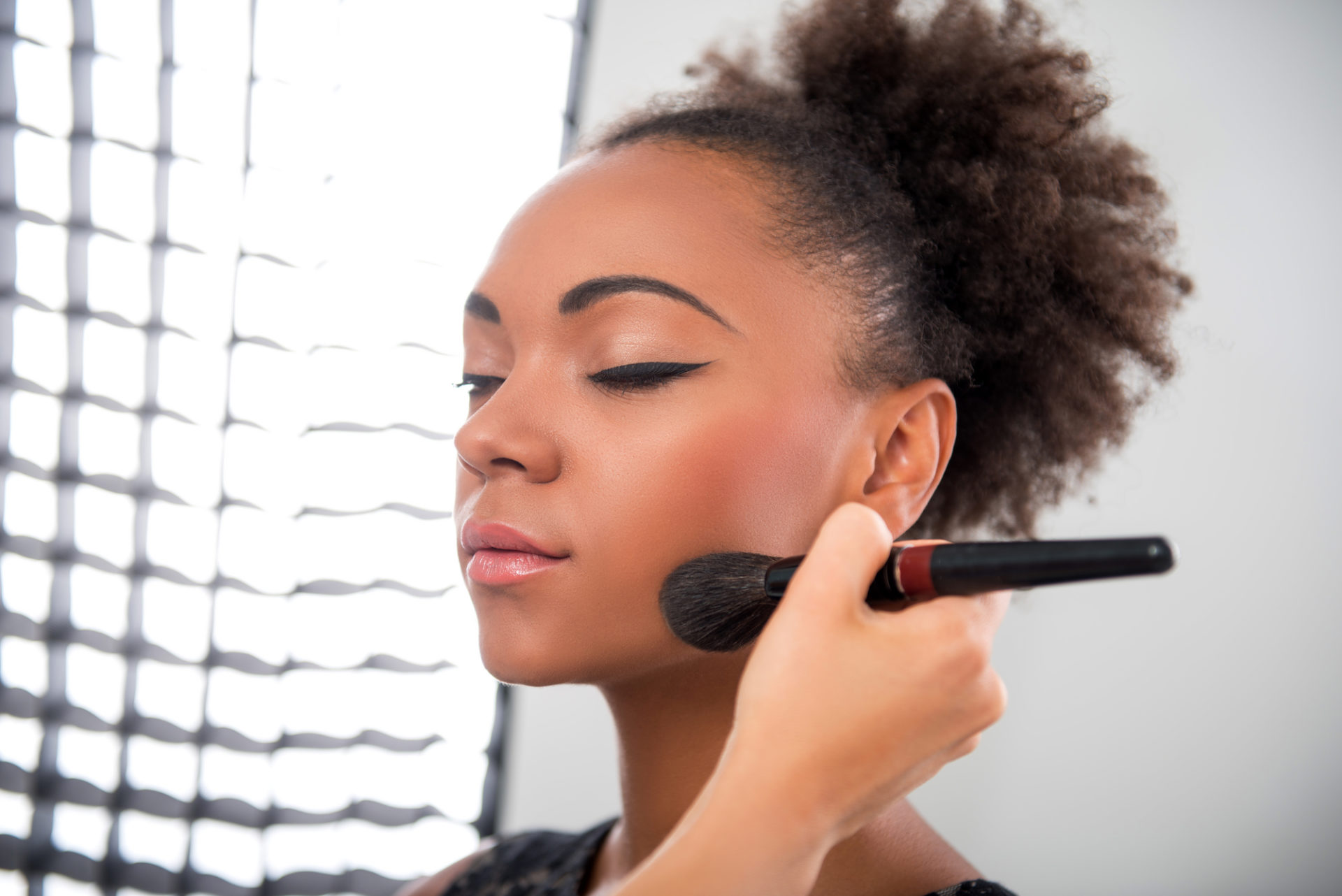 Makeup artist applying blush to a client in a lit studio