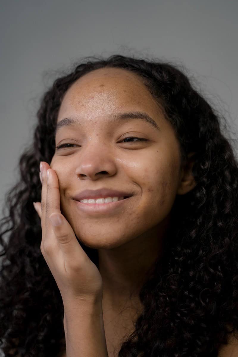 Smiling young woman with curly hair resting her hand on her cheek