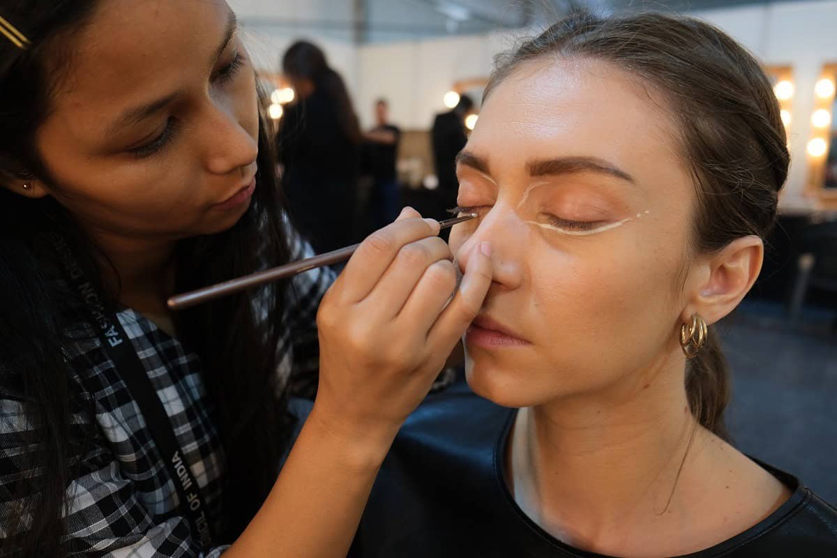 Makeup artist working on a model backstage in a busy dressing room