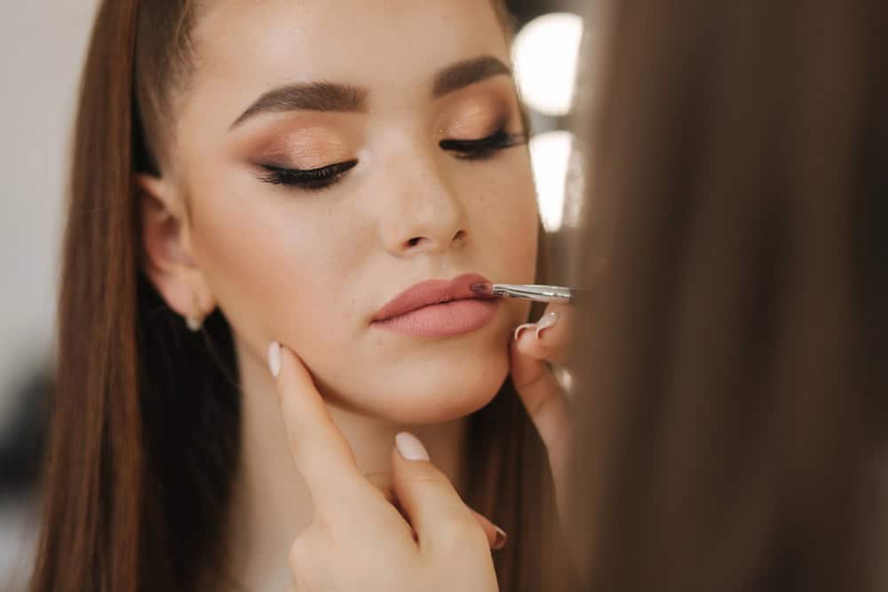 Makeup artist applying lip liner to a client in a studio