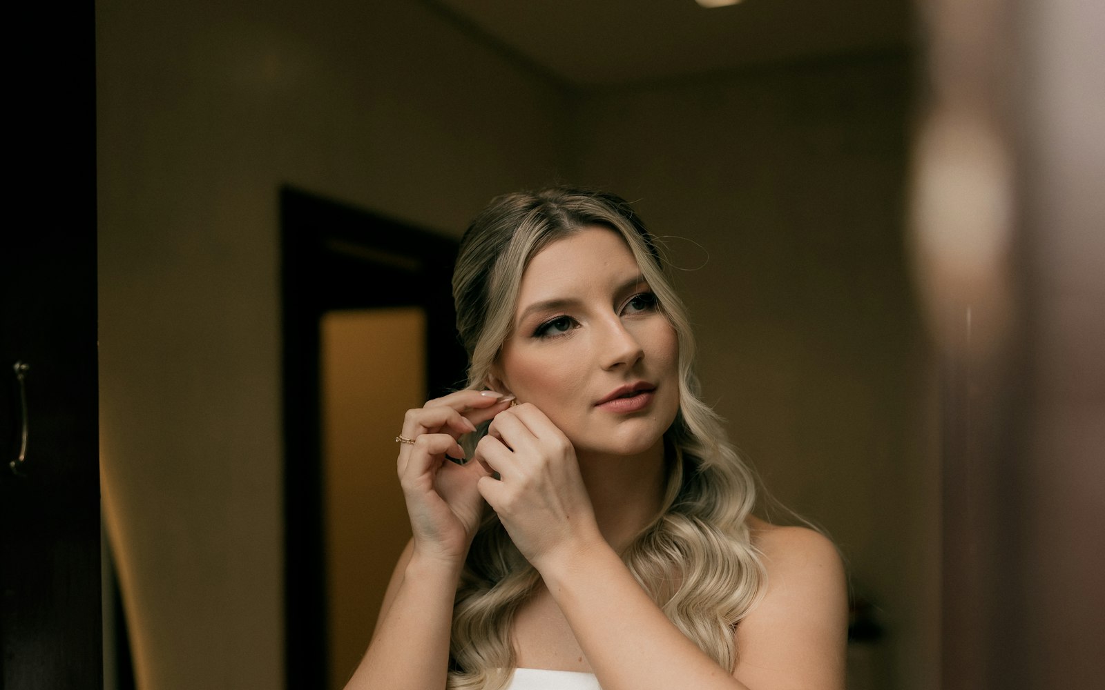 Bride putting on an earring in front of a mirror before the ceremony