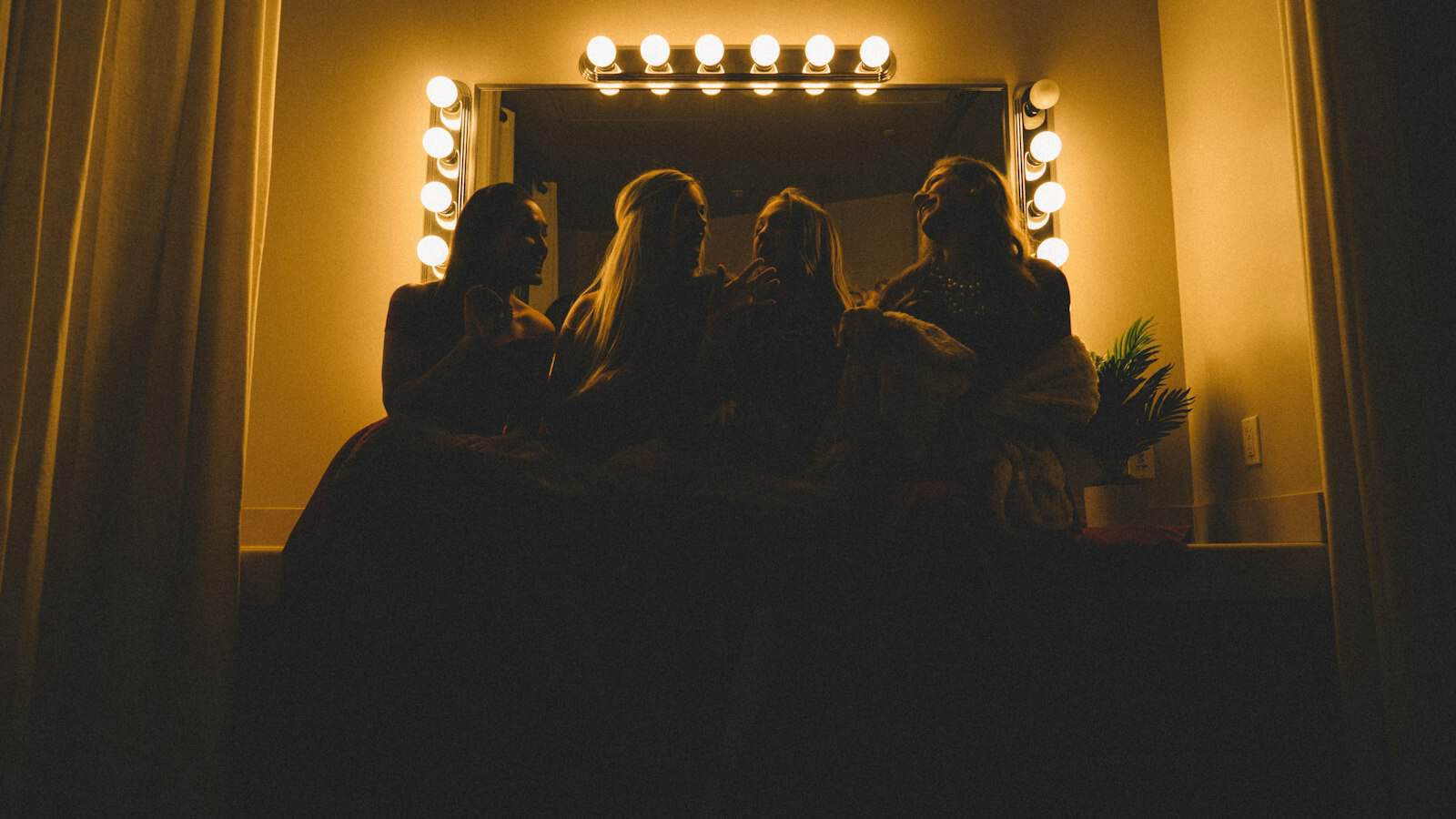 Performers seated at a lit dressing room mirror backstage