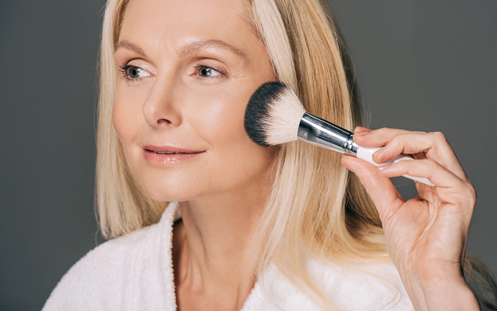 Older woman applying powder blush with a large brush