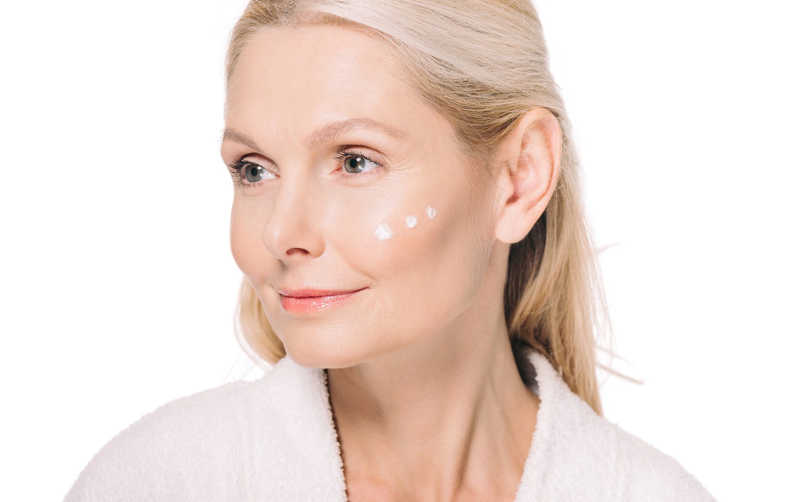 Older woman with dots of skin cream on her cheek before makeup