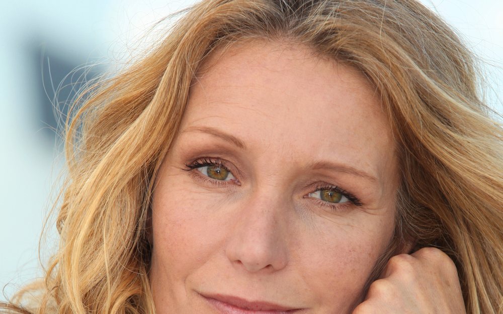 Middle-aged woman with wavy blonde hair resting her face on her hand
