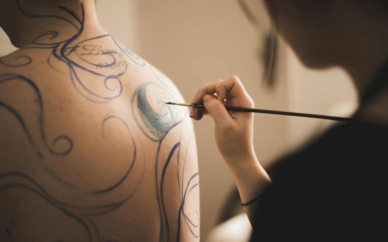 Artist painting a design across a model's back and shoulder