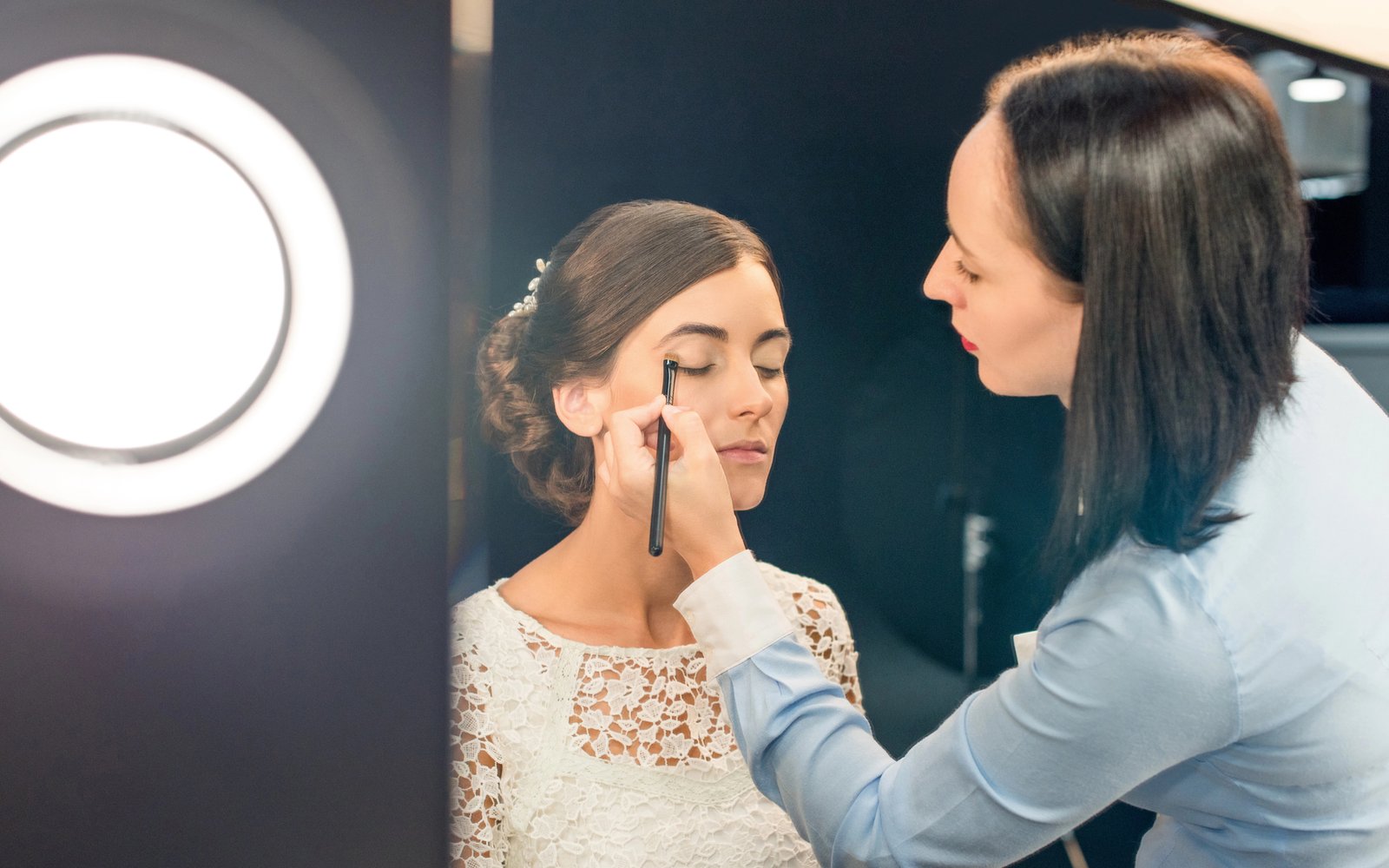 Makeup artist applying eyeshadow to a bride by a ring light
