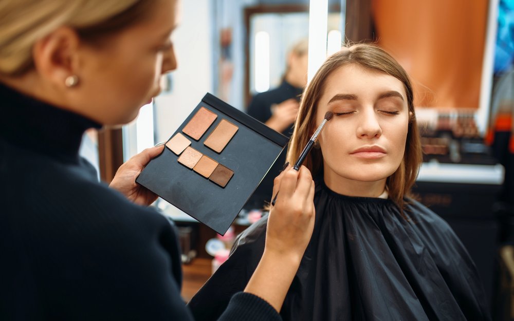 Makeup artist holding a palette while applying shadow to a client in a salon