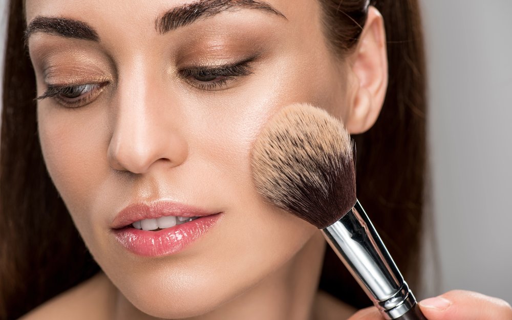 Close-up of a large brush applying powder to the cheek