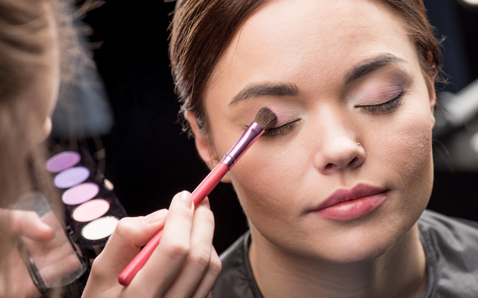 Artist sweeping lavender eyeshadow across a model's lid in the studio