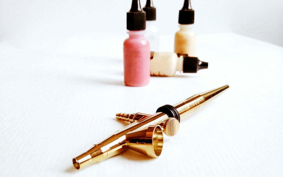 Gold airbrush lying beside small bottles of airbrush foundation