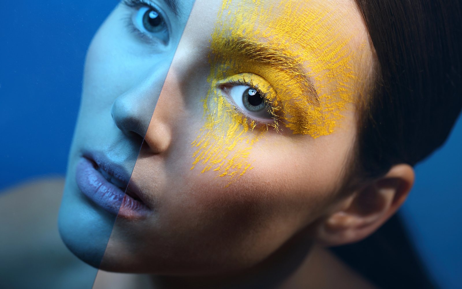 Model with half of her face painted blue and yellow pigment around one eye
