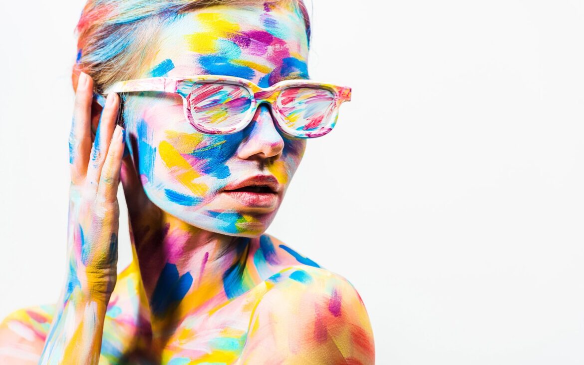 Model covered in bright multicolor body paint wearing painted sunglasses