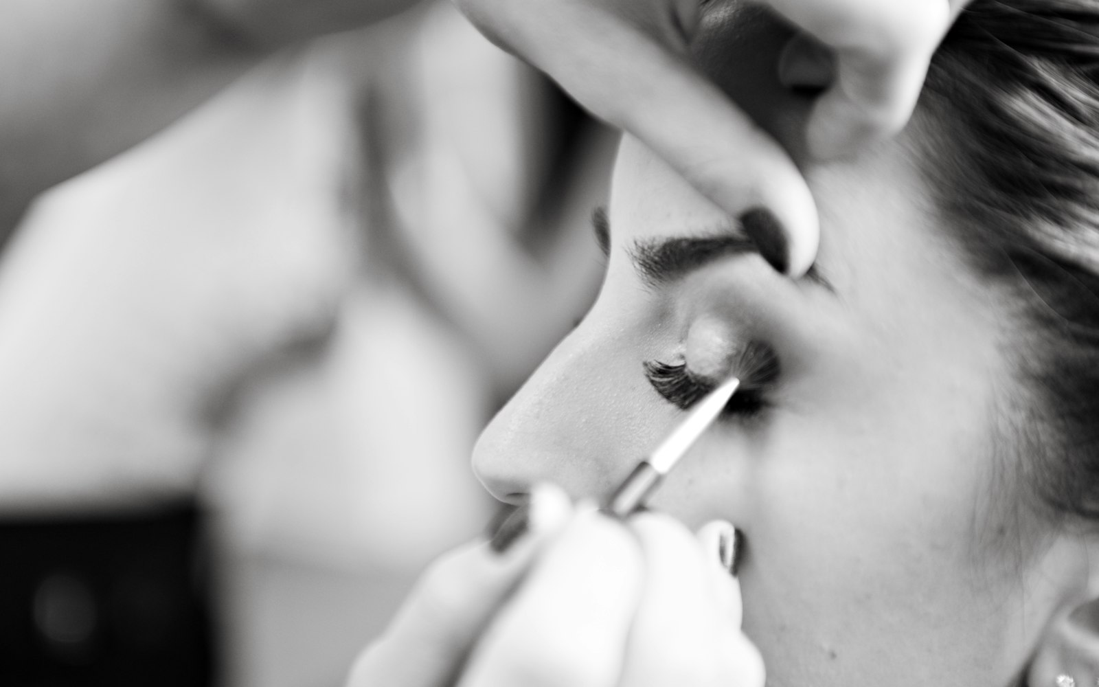 Close-up of eye makeup being applied with a fine brush, in black and white