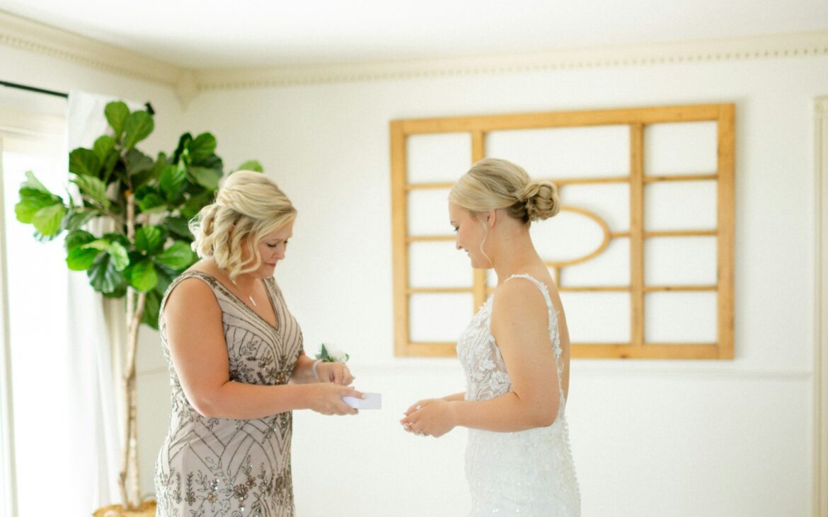 Bride in a lace gown getting ready with her mother in a bright room