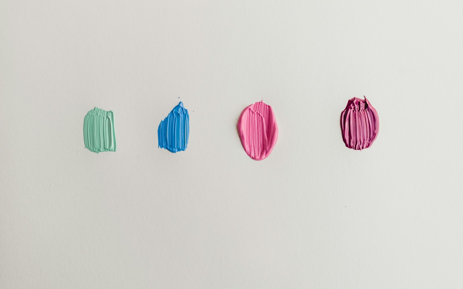 Four paint swatches in green, blue, pink and plum on white