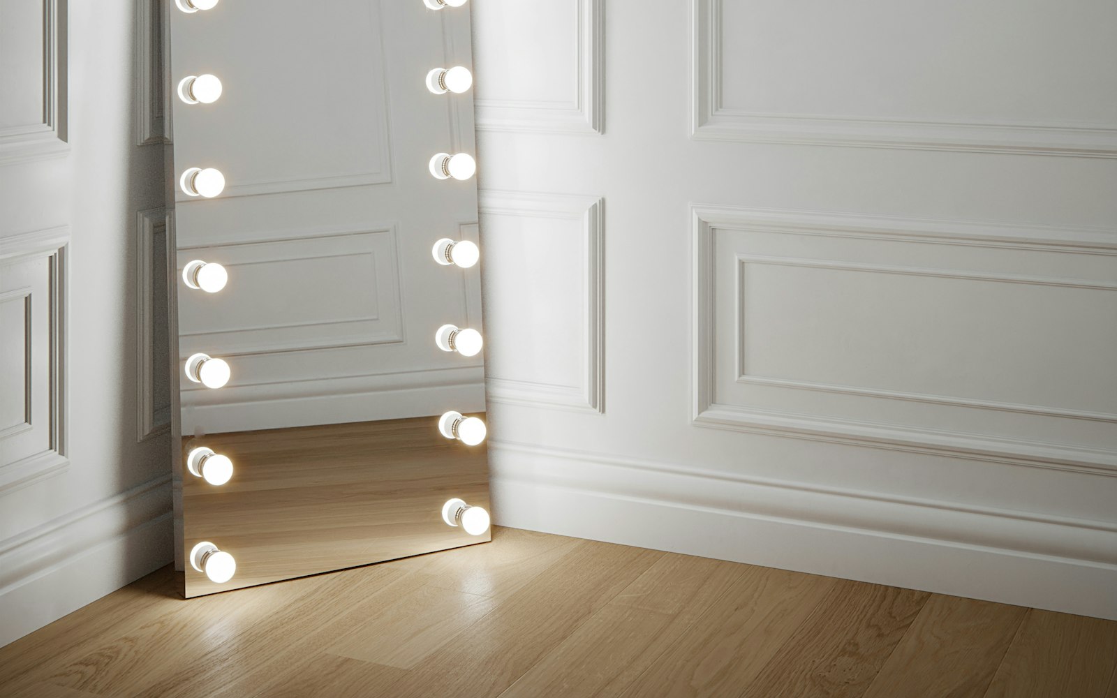 Full-length mirror framed with bulbs in a white room