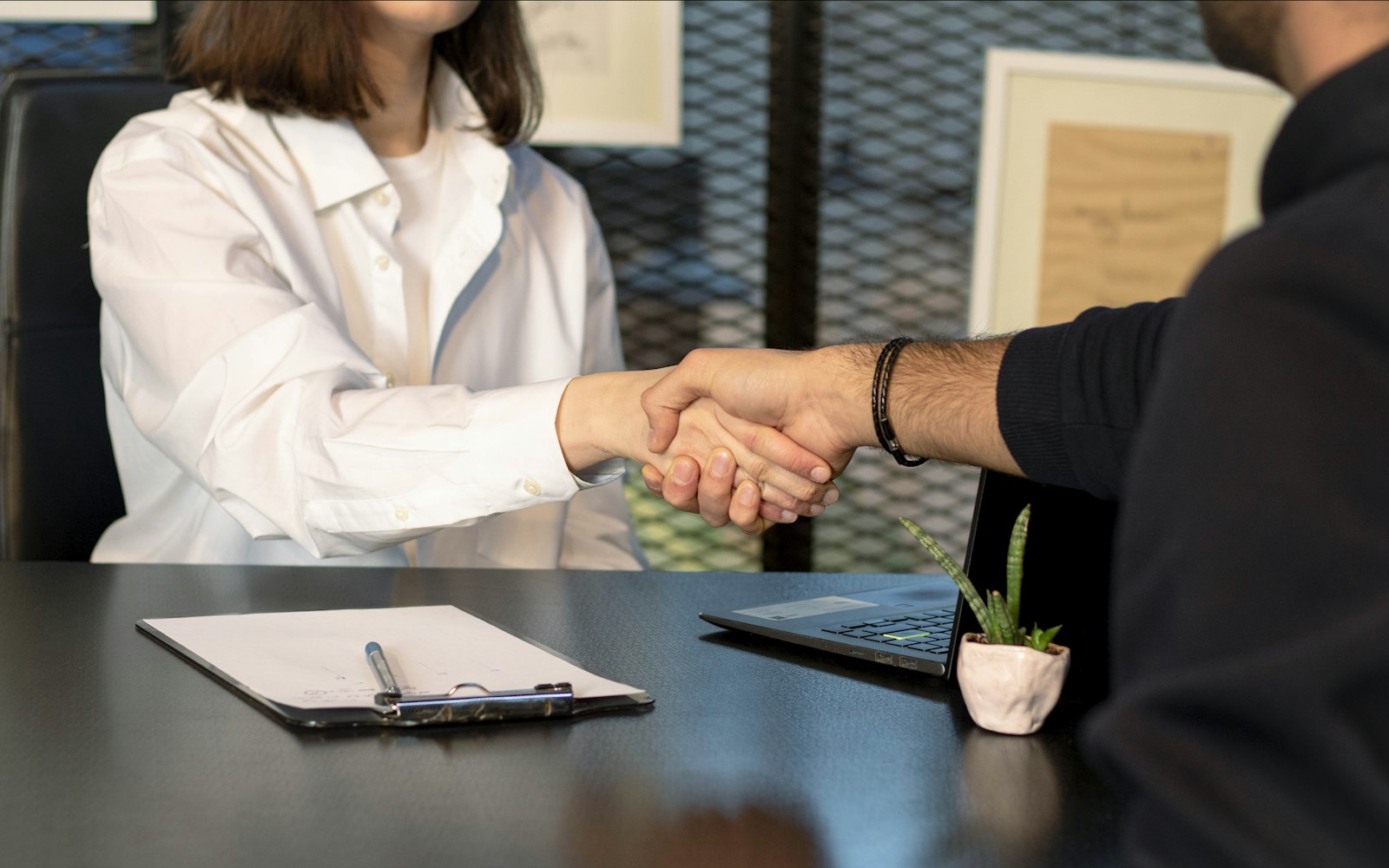 Handshake across a desk with a clipboard