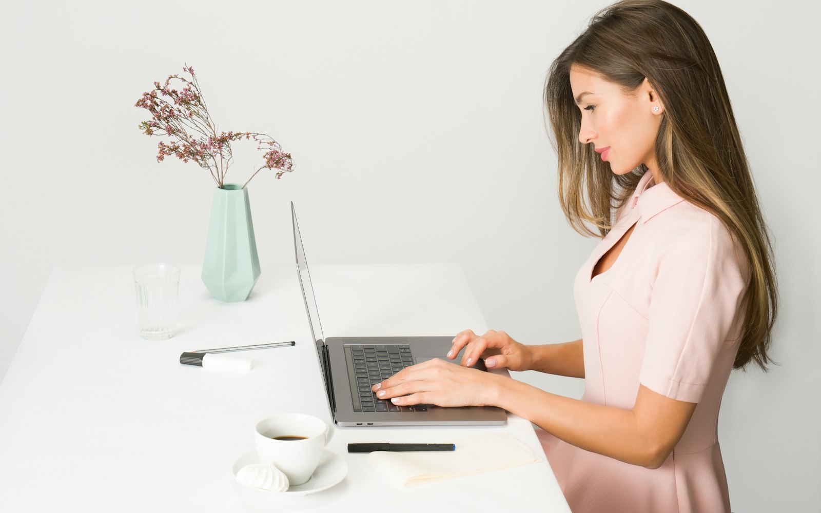 Woman typing on a laptop at a bright white desk