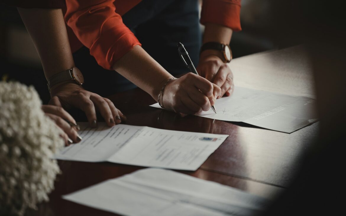 Two people signing printed agreements at a table
