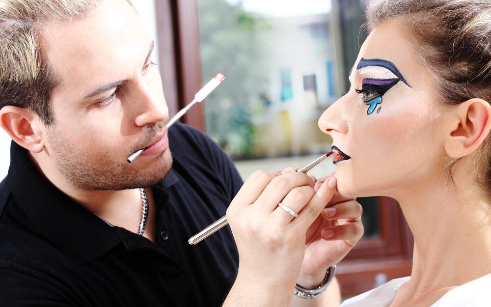Makeup artist applying lipstick to a model with a graphic black eye look