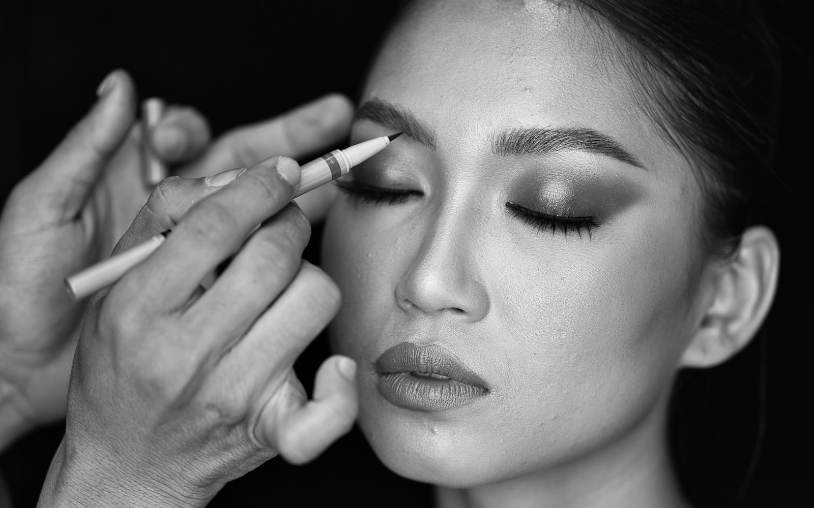 Makeup artist applying eyeliner to a model, in black and white