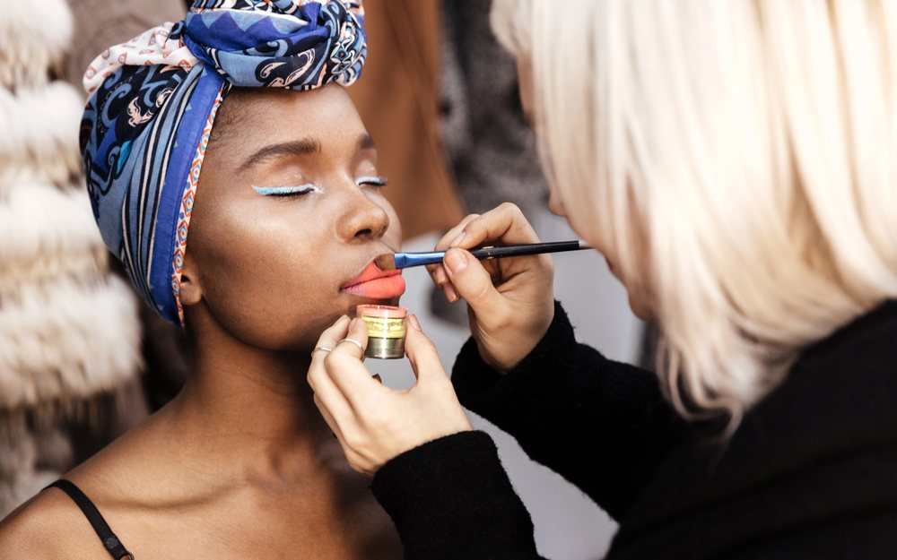 Makeup artist applying lip color with a brush in a studio