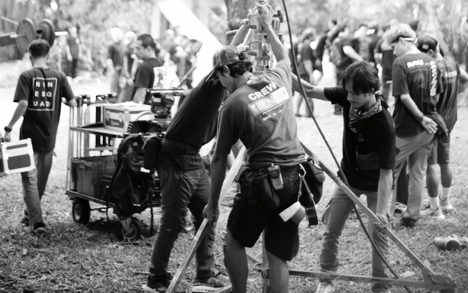 Film crew moving equipment on an outdoor location, in black and white