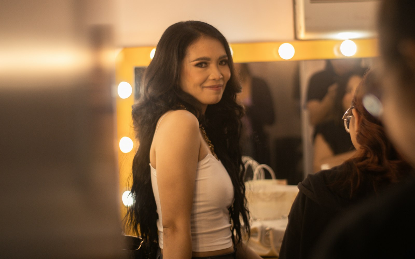Performer at a lit mirror while an artist prepares her hair