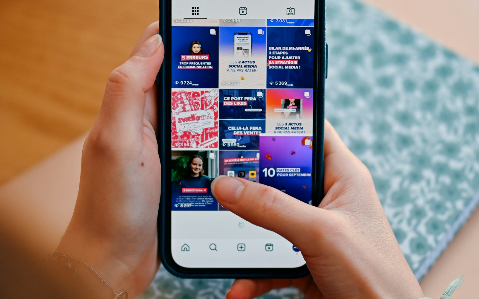 Hands holding a phone showing a grid of posts
