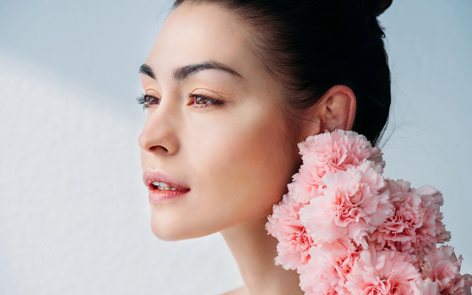 Model with fresh, dewy skin and pink flowers at her shoulder