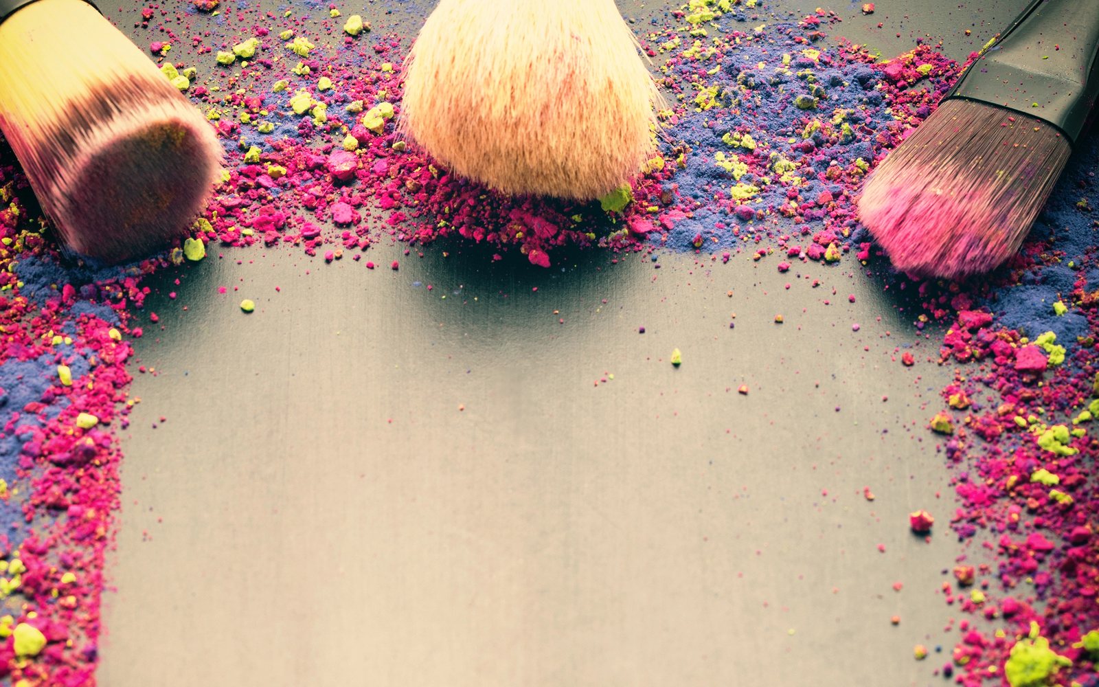 Makeup brushes on a background of scattered pink and blue pigment