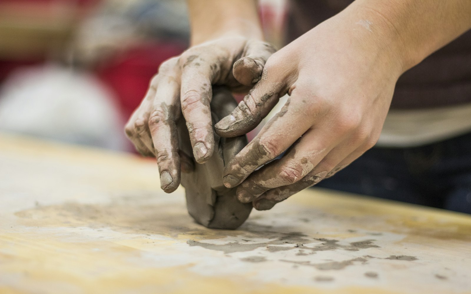 Hands kneading a lump of clay on a worktable