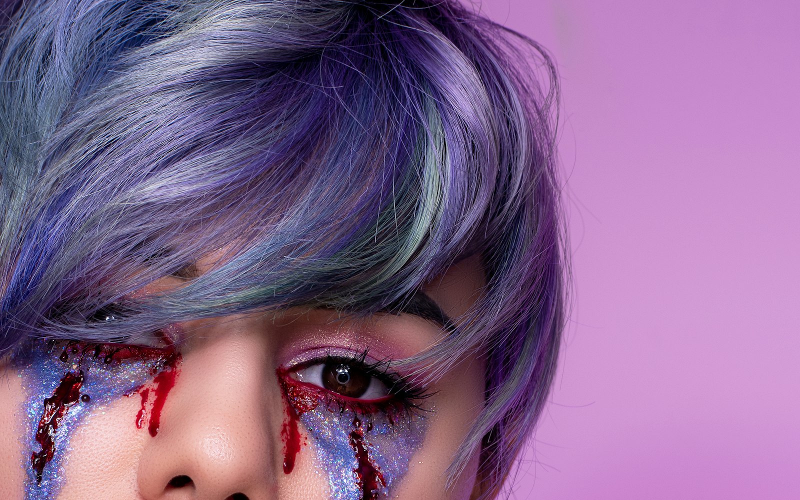 Close-up of stage blood running from the eye over violet glitter makeup