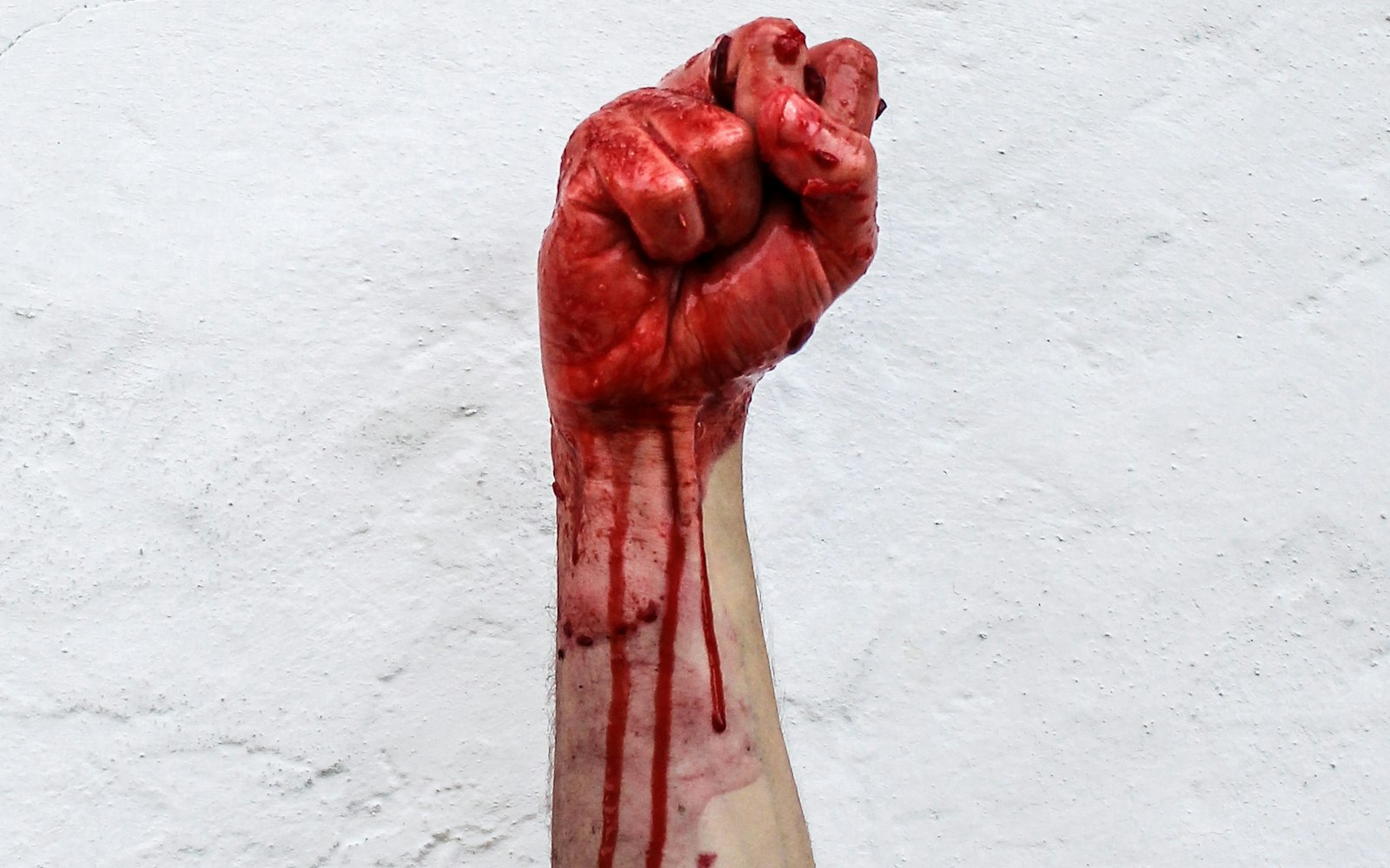 Raised fist dripping with stage blood against a white wall