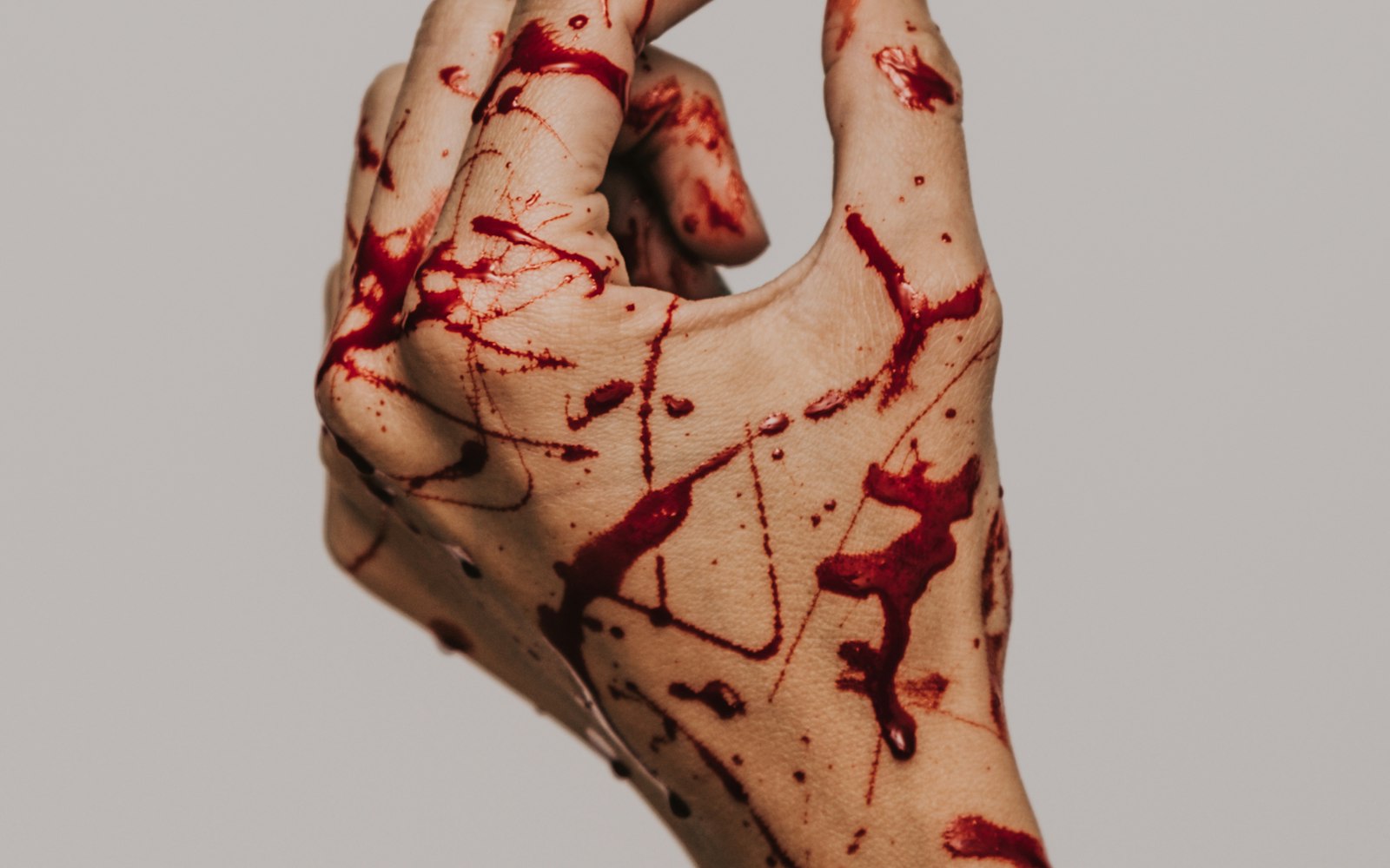 Hand covered in spattered stage blood against a pale wall