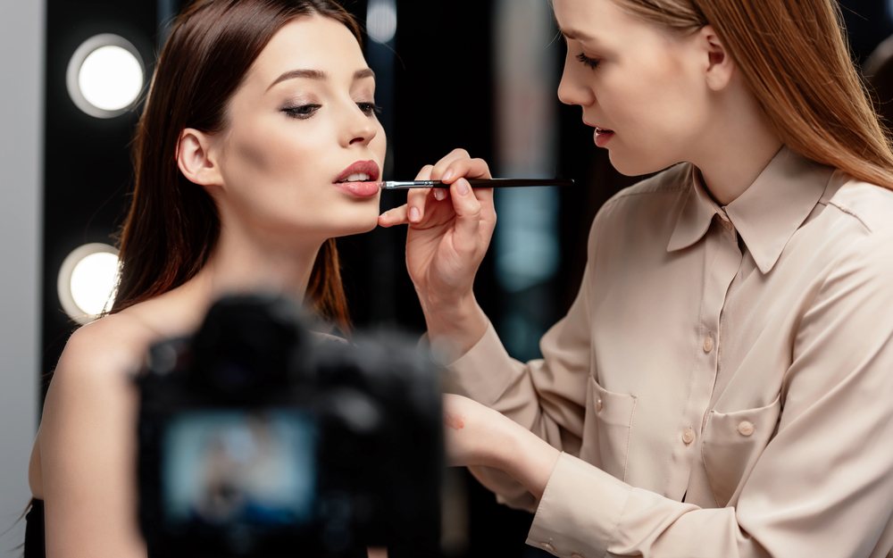 Makeup artist applying lip gloss to a model in front of a camera